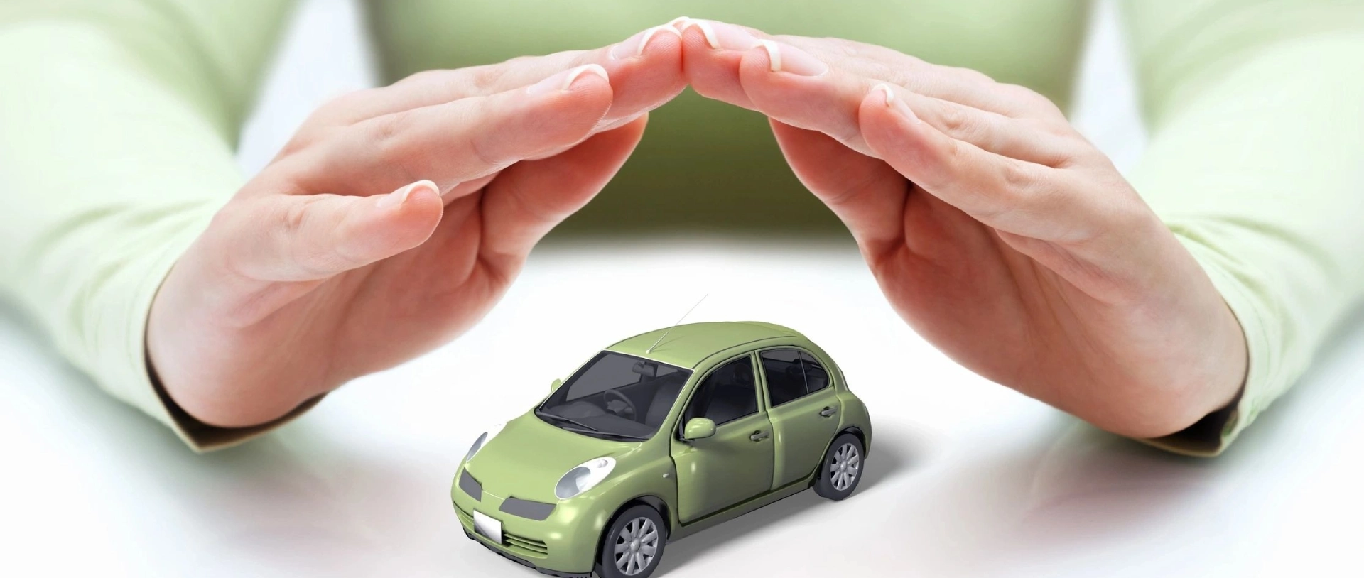 A green car is being protected by two hands.